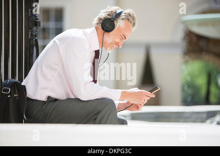 Businessman listening to headphones on city street Banque D'Images