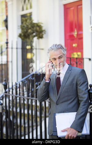 Businessman talking on cell phone sur avant stoop Banque D'Images