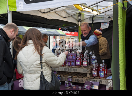 Gens touristes visiteurs et commerçant de marché homme vendant des bouteilles de sloe gin York North Yorkshire Angleterre Royaume-Uni Grande-Bretagne Banque D'Images