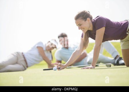 Femme regardant amis flick golf balle vers le trou Banque D'Images