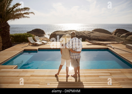 Senior couple hugging par piscine moderne donnant sur l'océan Banque D'Images