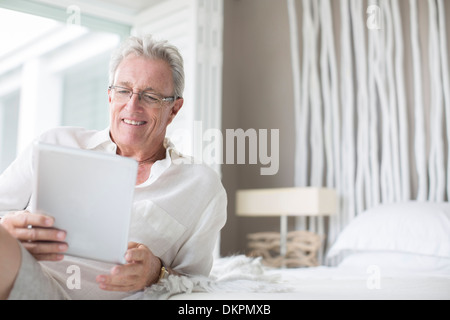 Older Man using digital tablet on bed Banque D'Images