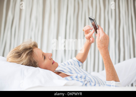 Femme plus âgée using cell phone on bed Banque D'Images