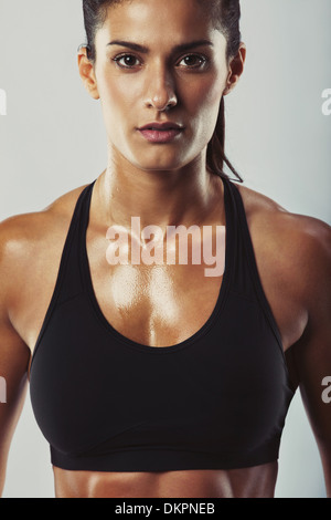 Close up image of young woman in sports bra looking at camera contre fond gris. Construction musculaire détendue femelle Banque D'Images