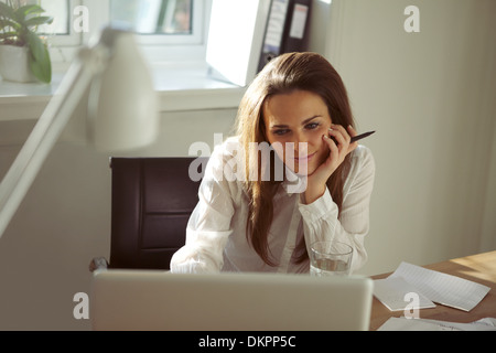 Belle jeune femme travaillant à la maison using laptop in home office. Pretty young businesswoman sitting at her desk using laptop Banque D'Images