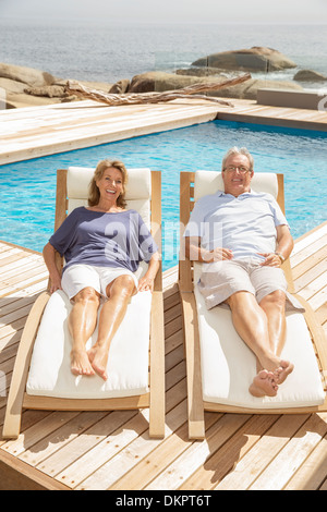 Couple portant sur les chaises longues au bord de la piscine Banque D'Images