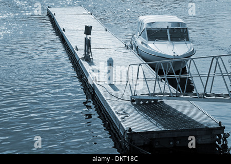 Petite embarcation à moteur flottant amarré près de la jetée en bois Banque D'Images