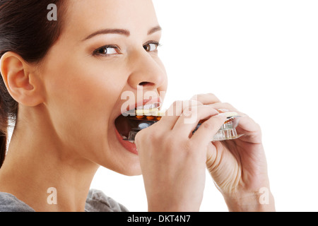 Belle femme occasionnels en essayant de manger emballage de comprimés. Isolé sur blanc. Banque D'Images