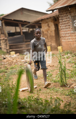 Course de l'enfant avec une roue dans des taudis ougandais - Gombe, l'Ouganda, l'Afrique de l'Est. Banque D'Images