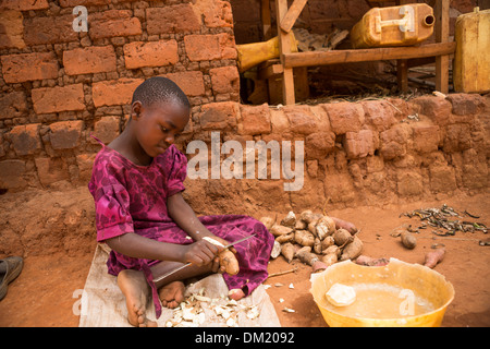 Pelures de pommes de terre d'un enfant devant son domicile à Gombe, l'Ouganda, l'Afrique de l'Est. Banque D'Images