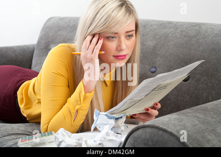 Très jolie jeune femme couchée sur un canapé tenant la paperasse. Banque D'Images