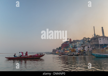 Un bateau plein de touristes femmes hindoues flotte sur le Gange sacré à Varanasi au coucher du soleil près de la gravure de Manikarnika ghat. Banque D'Images