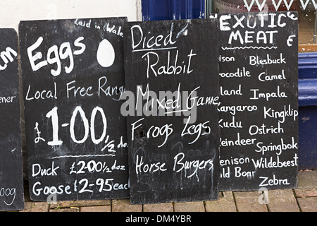 Tableau noir signe avec les viandes exotiques et les aliments énumérés avec des prix à l'extérieur d'un delicatessen, Galles, Royaume-Uni Banque D'Images