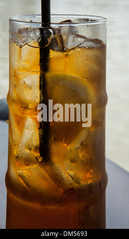 Un verre de thé glacé, avec de la glace, une tranche de citron et une paille noire. Banque D'Images