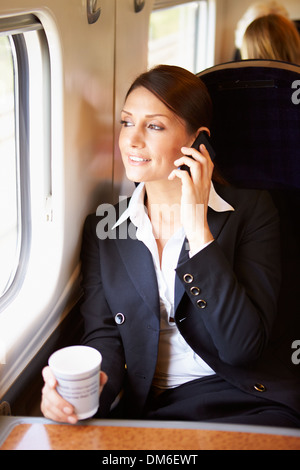 Banlieue femelle avec du café sur le train à l'aide de Mobile Phone Banque D'Images