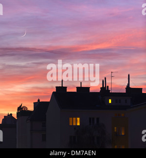 Coucher de soleil sur les toits en milieu urbain avec des lumières de certaines fenêtres d'accueil Banque D'Images