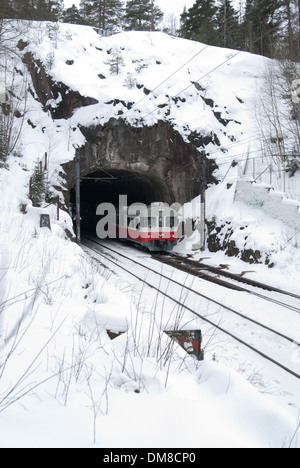 Train en direction d'un petit tunnel sous un grand rock formation sur une journée d'hiver enneigée Banque D'Images