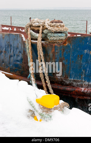 Épave attaché avec des cordes épaisses à jaune bollard en neige à quay Banque D'Images