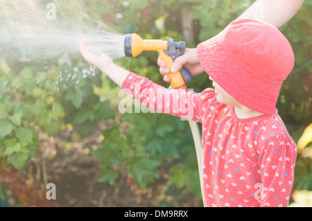 Scène d'été de style de vie. Petite fille jouant avec deux parents dans le jardin, se sentir l'eau du réseau sprinkleur Banque D'Images