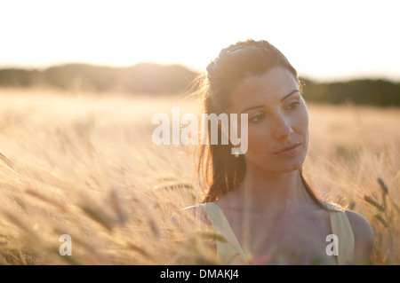 Young woman in dress debout dans un champ de maïs au coucher du soleil Banque D'Images