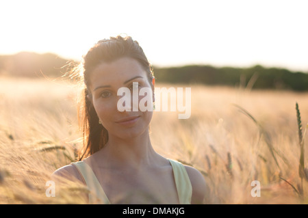 Young woman in dress debout dans un champ de maïs au coucher du soleil Banque D'Images