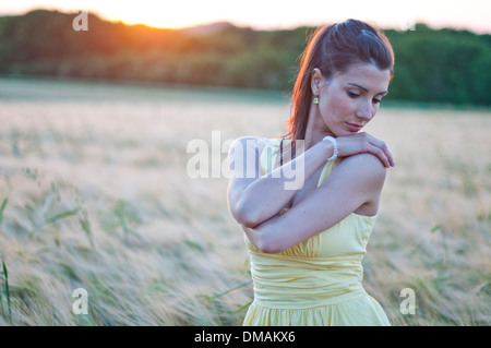 Jeune femme triste debout dans un champ de maïs au coucher du soleil Banque D'Images