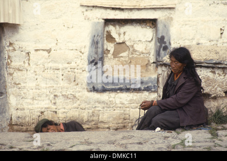 Une pauvre vieille femme assise dans une rue de Lhassa, Tibet, Chine. Un jeune homme se cache de l'appareil photo. Banque D'Images