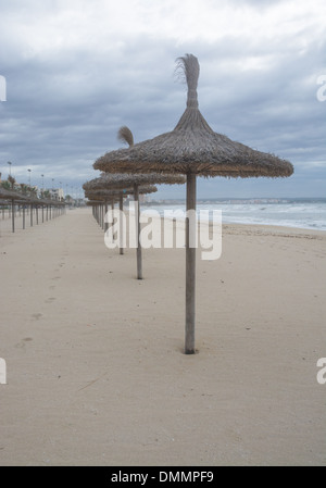 Des parasols de paille dans une rangée sur sable avec empreintes de pieds Banque D'Images