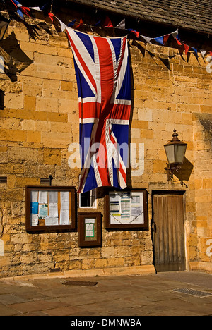 Bâtiment en pierre avec une grande Union Jack, drapeau de Grande-bretagne accrochée à l'avant-toit de la halle de la ville de marché de Cotswolds Chipping Campden. Banque D'Images