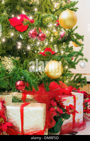 Arbre de Noël décoré avec des lumières scintillantes Poinsettia Ornements Snowflakes avec les cadeaux emballés sous l'arbre Banque D'Images