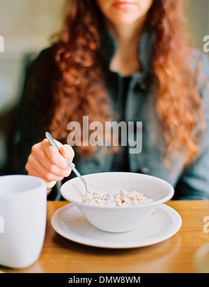 Une femme de manger les céréales petit déjeuner d'un bol blanc. Banque D'Images