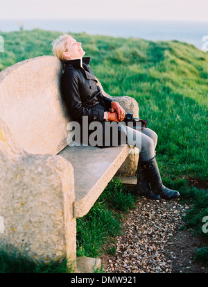 Une femme assise sur un banc en pierre sur un chemin côtier. Banque D'Images