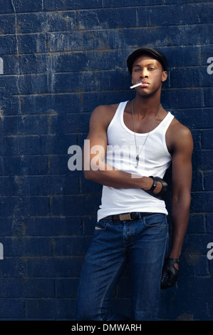 Beau black, African American man leaning against wall fumer, porter un jean bleu et de crieur, un concept de mode vintage Banque D'Images