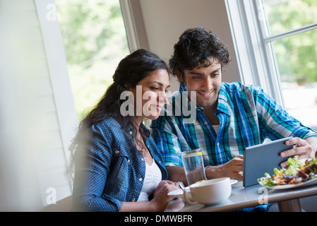 Un couple assis à la tablette numérique à un. Banque D'Images