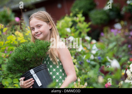Une pépinière de fleurs biologiques. Une jeune fille portant une plante dans un pot. Banque D'Images