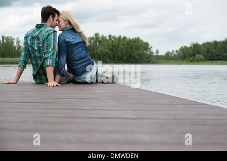 Un homme et une femme assis sur une jetée par un lac. Banque D'Images