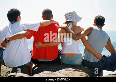 Vue arrière de quatre amis avec les bras autour de chaque ou assis dans une rangée. Banque D'Images