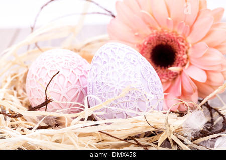 Belle couleur pastel oeufs de Pâques en bonneterie complexes artisanaux avec un frais couvre Gerbera rose daisy dans un nid de paille propre pour une célébration de Pâques symbolique traditionnelle Banque D'Images