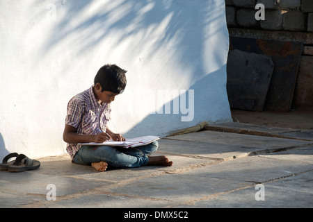 Jeune Indien garçon faire le travail scolaire en dehors de son village de l'Inde rurale accueil. L'Andhra Pradesh, Inde Banque D'Images