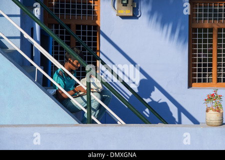 Teenage Indian boy sitting on steps faisant des travaux scolaires à l'extérieur de sa maison village avec les ombres. L'Andhra Pradesh, Inde Banque D'Images