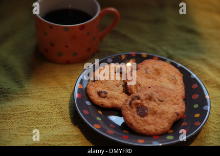 Une tasse de café noir avec trois cookies aux pépites de chocolat sur une plaque à pois Banque D'Images