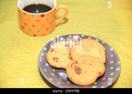 Une tasse de café noir avec trois cookies aux pépites de chocolat sur une plaque à pois Banque D'Images