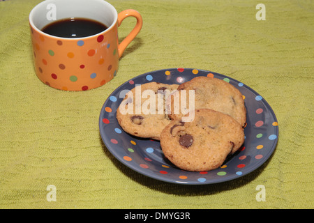 Une tasse de café noir avec trois cookies aux pépites de chocolat sur une plaque à pois Banque D'Images