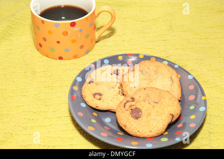 Une tasse de café noir avec trois cookies aux pépites de chocolat sur une plaque à pois Banque D'Images