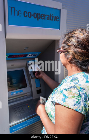 Middle-aged Hispanic woman withdrawing l'argent d'une banque coopérative ATM machine en Angleterre, FR, UK. Banque D'Images