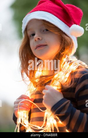 Une petite fille vêtue d'un chapeau de Père Noël et de la féerie de lumières de Noël Banque D'Images