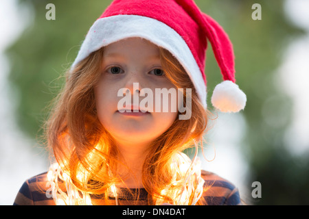 Une petite fille vêtue d'un chapeau de Père Noël et de la féerie de lumières de Noël Banque D'Images