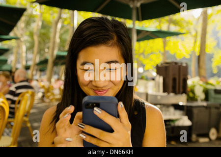 Chinese girl using cell phone on restaurant patio Banque D'Images