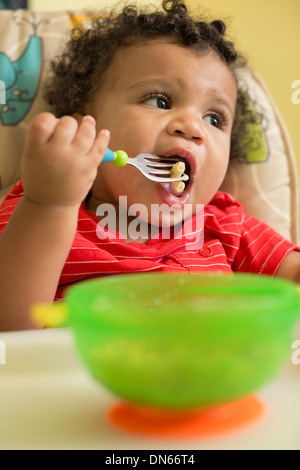 Mixed Race bébé garçon manger dans une chaise haute Banque D'Images