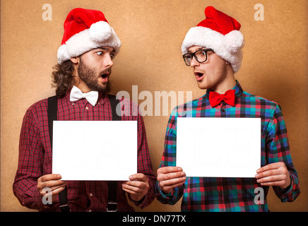 Noël, x-mas, les gens, la publicité, la vente concept - deux heureux homme à Santa helper hat avec tableau blanc vierge. Style hippie. Banque D'Images